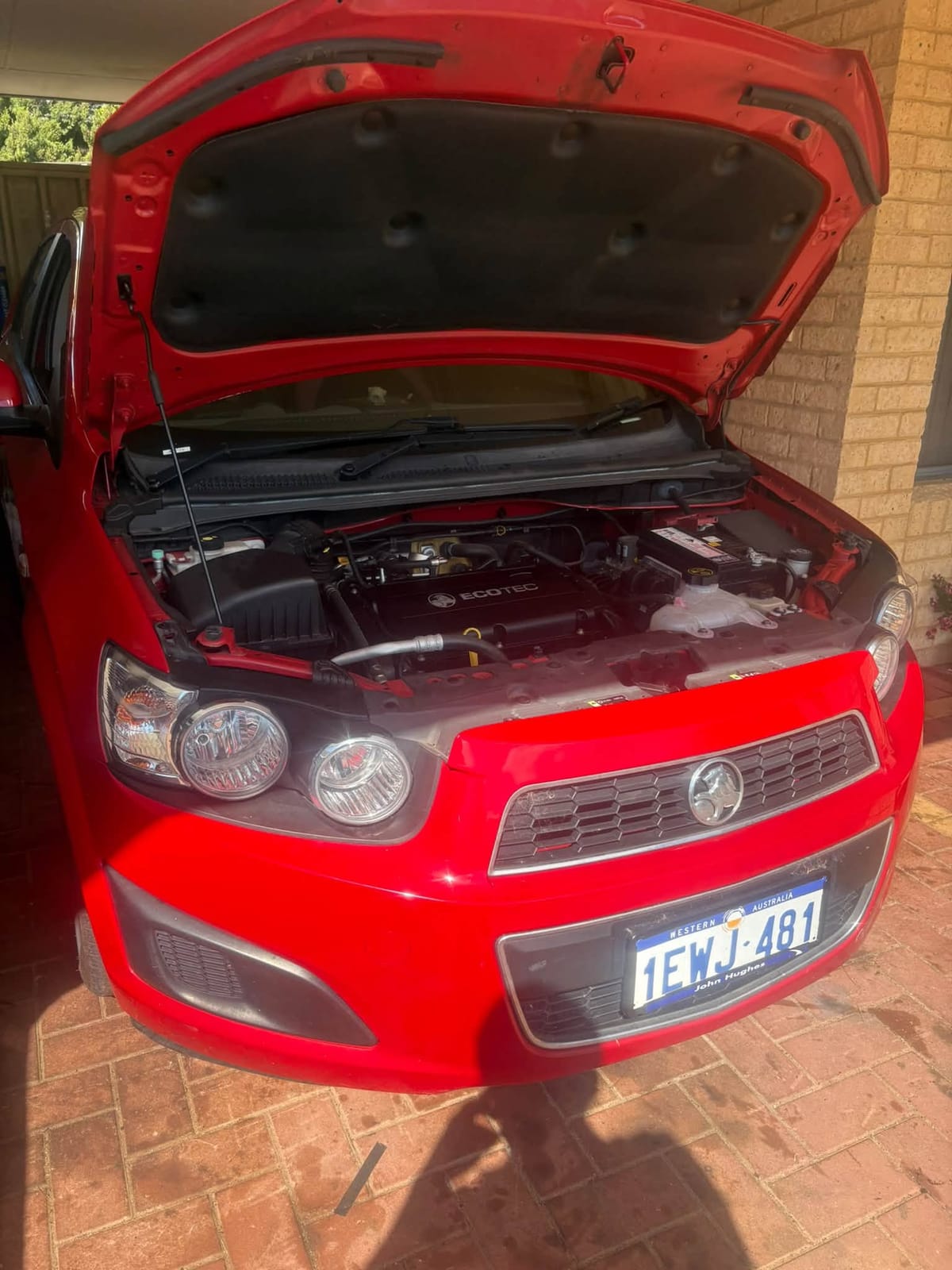 Red Holden Barina in a driveway with the bonnet open