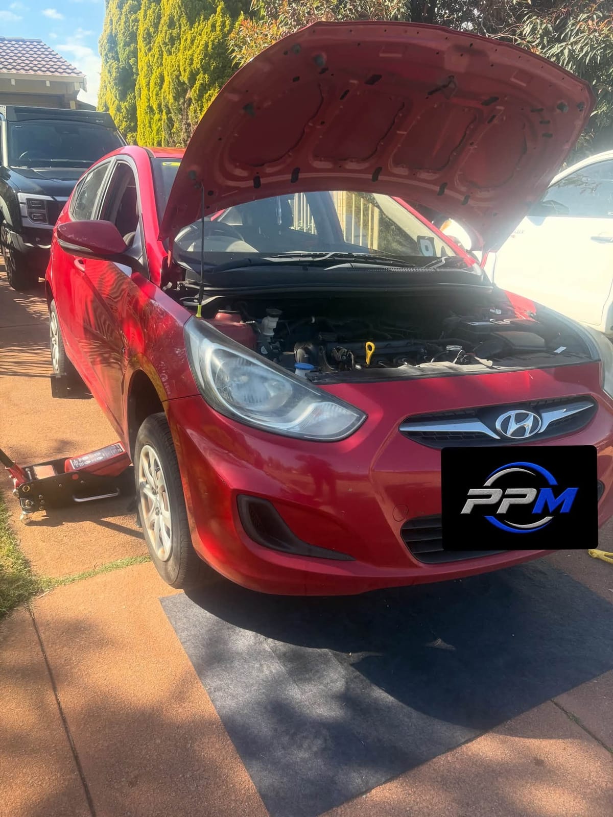 Red Hyundai on jacks in a driveway with the bonnet open during a service