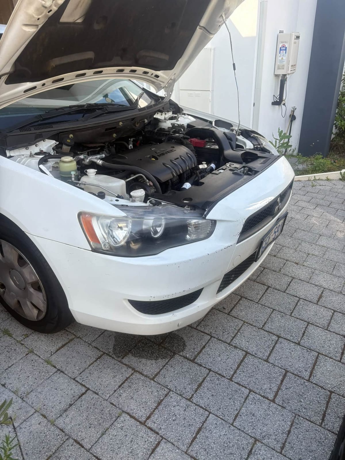 White Mitsubishi Lancer with the bonnet open on paving