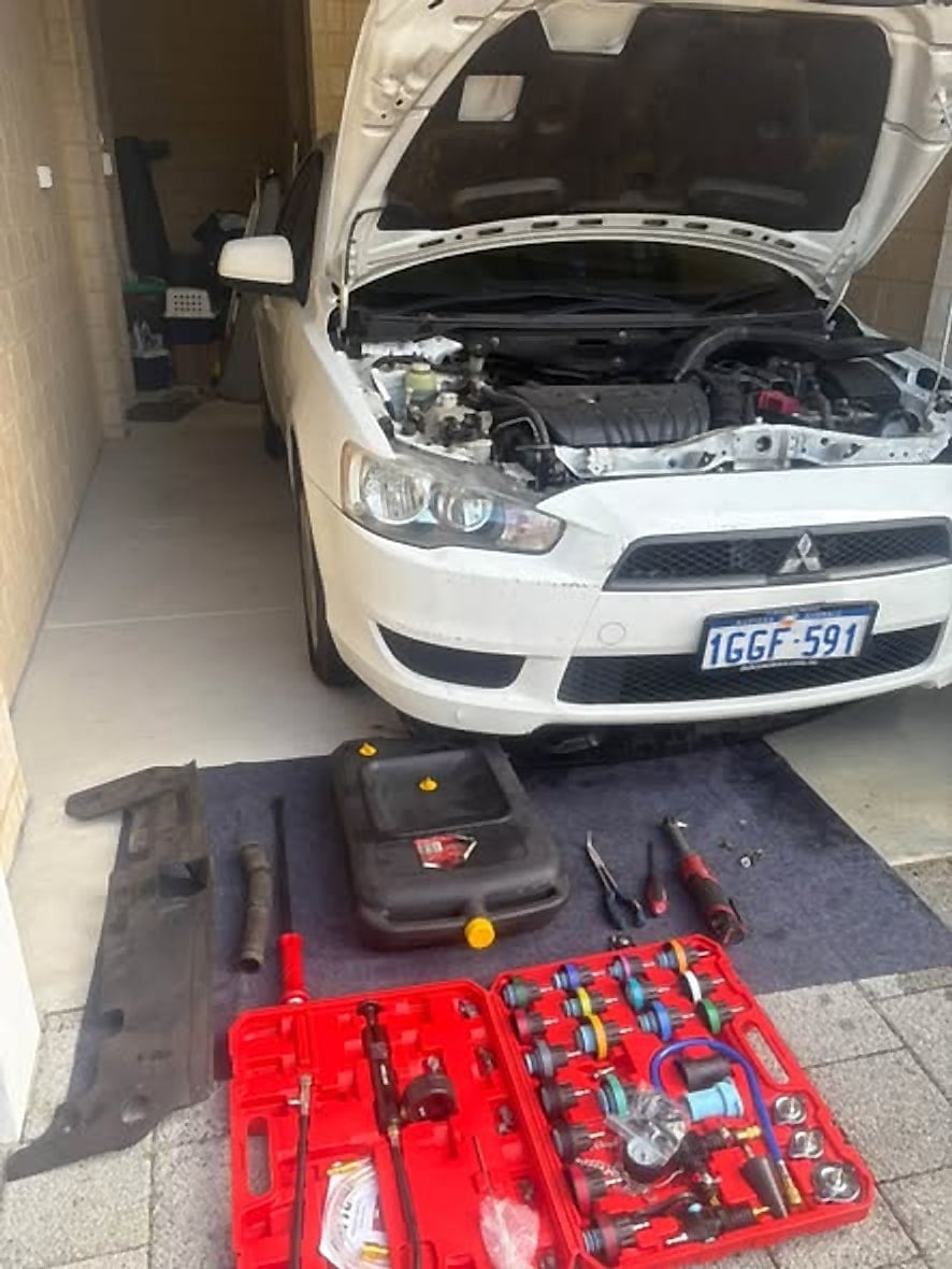 White Mitsubishi Lancer in a garage with the bonnet open and tools laid out on a mat