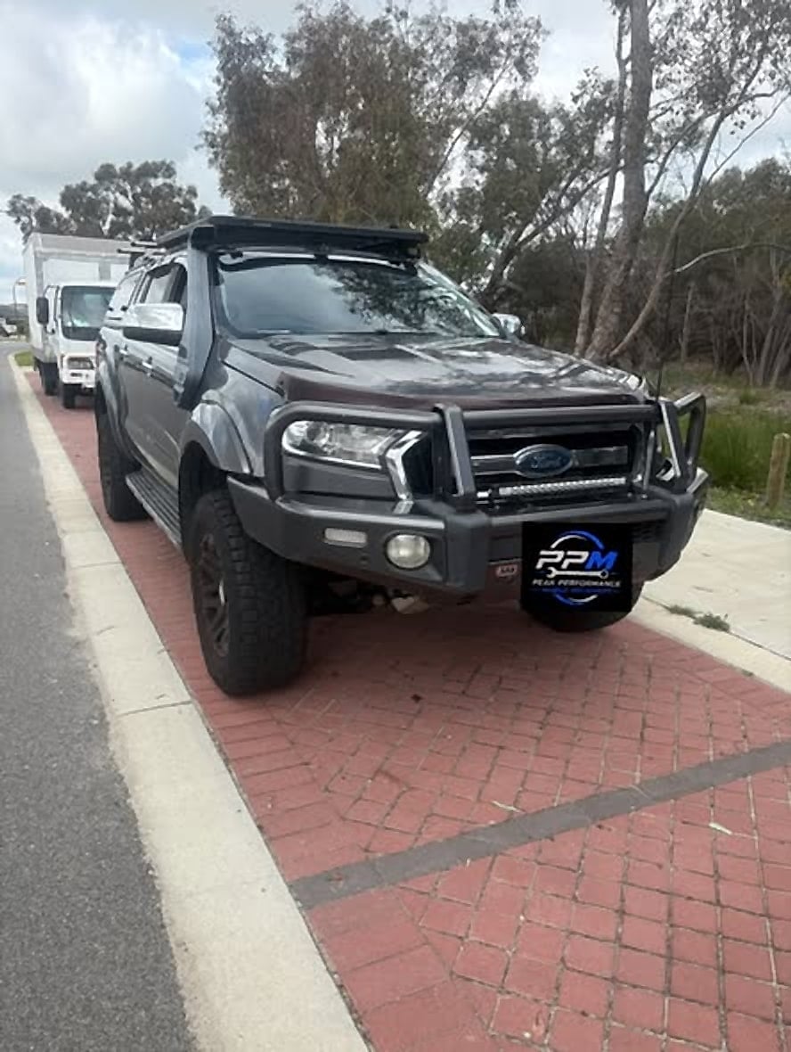 Dark Ford Ranger on a red paved street with the Peak Performance plate